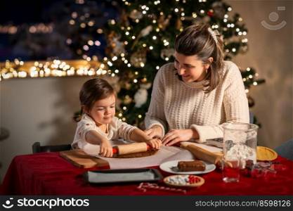 family, cooking and winter holidays concept - happy mother and baby daughter with rolling pin making gingerbread cookies from dough at home on christmas. mother and daughter making gingerbread at home