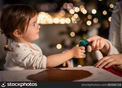 family, cooking and winter holidays concept - happy mother and baby daughter with mold making gingerbread cookies from dough at home on christmas. mother and daughter making gingerbread at home
