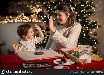 family, cooking and winter holidays concept - happy mother and baby daughter with rolling pin and dough for gingerbread cookies making high five gesture at home on christmas. mother and daughter making gingerbread at home