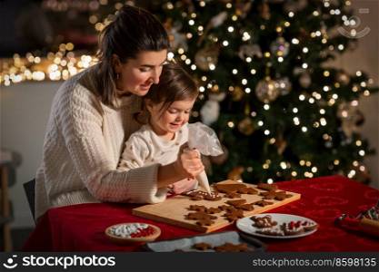 family, cooking and winter holidays concept - happy mother and baby daughter decorating gingerbread cookies at home on christmas. mother and daughter decorating gingerbread at home
