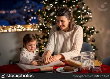 family, cooking and winter holidays concept - happy mother and baby daughter having fun with dough for gingerbread cookies at home on christmas. mother and daughter making gingerbread at home