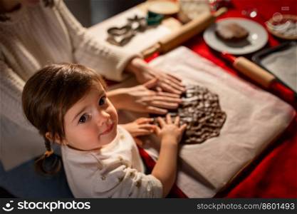 family, cooking and winter holidays concept - happy mother and baby daughter having fun with dough for gingerbread cookies at home on christmas. mother and daughter making gingerbread at home