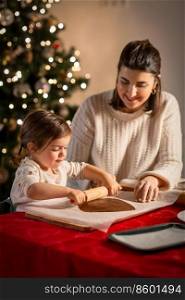 family, cooking and winter holidays concept - happy mother and baby daughter with rolling pin making gingerbread cookies from dough at home on christmas. mother and daughter making gingerbread at home