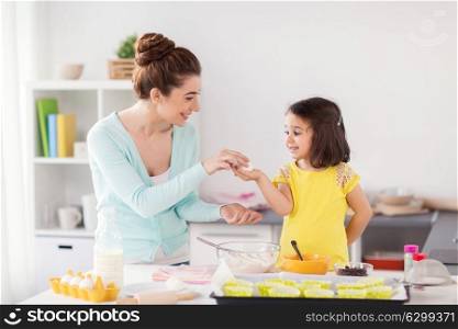 family, cooking, baking and people concept - happy mother and little daughter holding egg and making cupcakes at home kitchen. happy mother and daughter baking at home