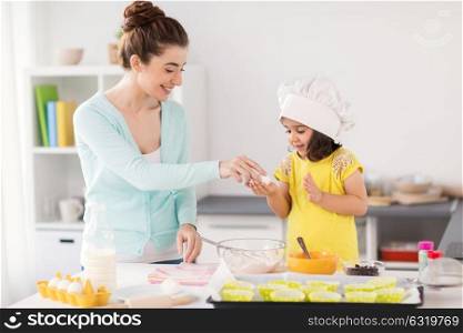 family, cooking, baking and people concept - happy mother and little daughter holding egg and making cupcakes at home kitchen. happy mother and daughter baking at home