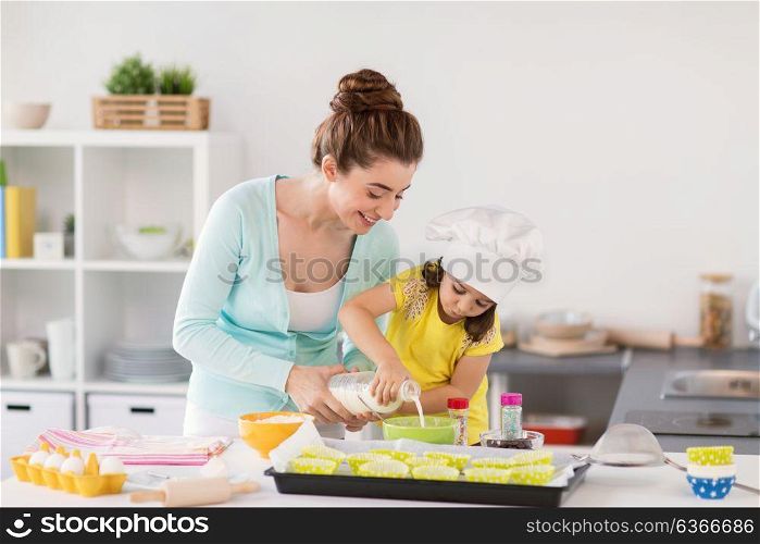 family, cooking, baking and people concept - happy mother and little daughter pouring milk into bowl and making dough for muffins at home kitchen. happy mother and daughter baking cupcakes at home