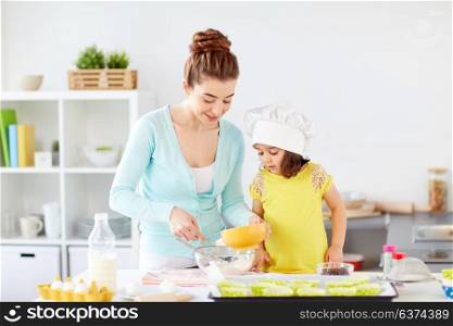 family, cooking, baking and people concept - happy mother and little daughter in chefs toque making batter for muffins at home kitchen. happy mother and daughter making dough at home