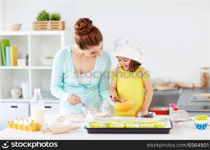 family, cooking, baking and people concept - happy mother and little daughter making batter for muffins at home kitchen. happy mother and daughter baking muffins at home
