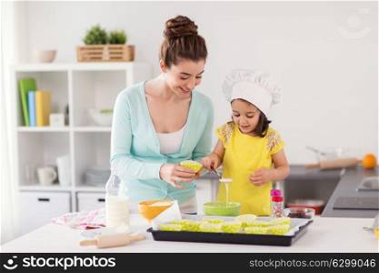 family, cooking, baking and people concept - happy mother with cupcake liner and little daughter with spoon pouring batter and making muffins at home kitchen. happy mother and daughter baking cupcakes at home