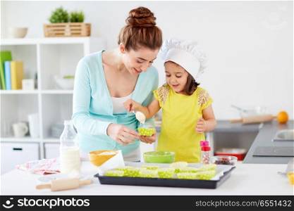 family, cooking, baking and people concept - happy mother with cupcake liner and little daughter with spoon pouring batter and making muffins at home kitchen. happy mother and daughter baking cupcakes at home. happy mother and daughter baking cupcakes at home