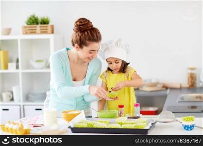 family, cooking, baking and people concept - happy mother with little daughter adding chocolate to cupcake liner and making muffins at home kitchen. happy mother and daughter baking cupcakes at home