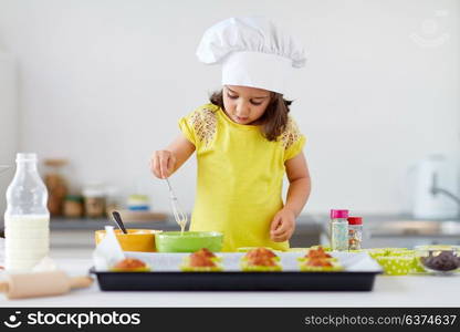 family, cooking, baking and people concept - little girl in chefs toque making batter for muffins or cupcakes at home kitchen. little girl in chefs toque baking muffins at home