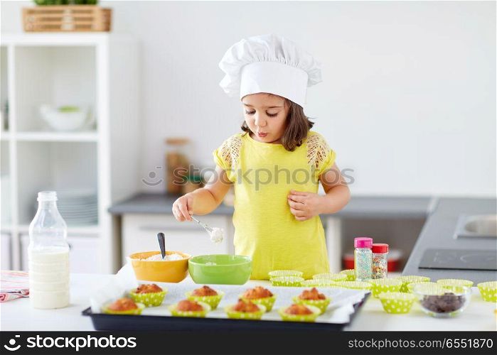 family, cooking, baking and people concept - little girl in chefs toque making batter for muffins or cupcakes at home kitchen. little girl in chefs toque baking muffins at home. little girl in chefs toque baking muffins at home