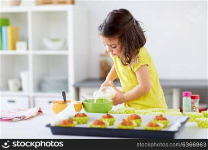 family, cooking, baking and people concept - little girl making batter for muffins or cupcakes and adding milk at home kitchen. little girl baking muffins at home