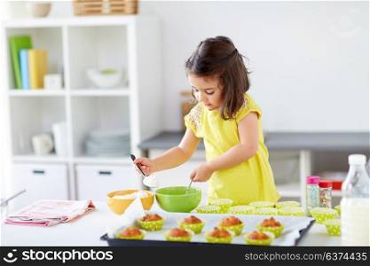 family, cooking, baking and people concept - little girl making batter for muffins or cupcakes at home kitchen. little girl baking muffins at home