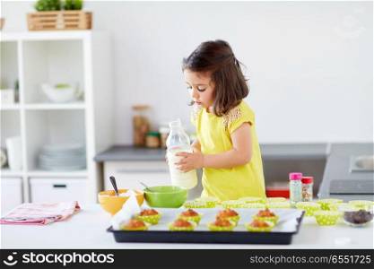 family, cooking, baking and people concept - little girl making batter for muffins or cupcakes and adding milk at home kitchen. little girl baking muffins at home. little girl baking muffins at home