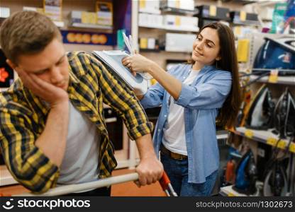 Family couple choosing electric iron in electronics store. Man and woman buying home electrical appliances in market. Couple choosing electric iron in electronics store