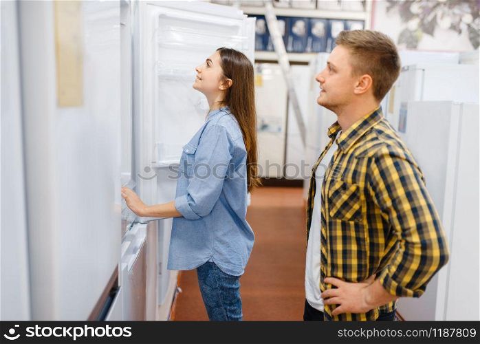 Family couple choosing refrigerator in electronics store. Man and woman buying home electrical appliances in market. Couple choosing refrigerator in electronics store