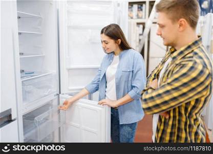 Family couple choosing refrigerator in electronics store. Man and woman buying home electrical appliances in market. Couple choosing refrigerator in electronics store