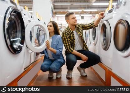 Family couple choosing washing machine in electronics store. Man and woman buying home electrical appliances in market. Couple choosing washing machine, electronics store