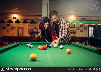 Family couple learn to play billiard, poolroom on background. Man and woman leisures, american pool game in sport bar, female player aiming to shot