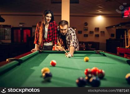 Family couple plays in billiard room. Man and woman leisures, american pool game in sport bar, male player aiming to shot. Family couple plays in billiard room