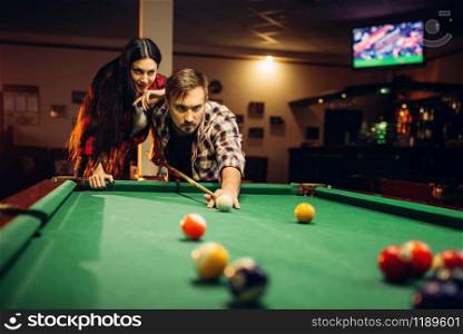 Family couple plays in billiard room. Man and woman leisures, american pool game in sport bar, male player aiming to shot