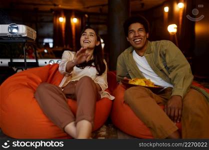 Family couple watching television projector on soft bag in living room. Movie night at home. Family couple watching television projector at home