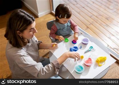 family, creativity and craft concept - mother and little daughter playing with modeling clay at home. mother and daughter playing with modeling clay
