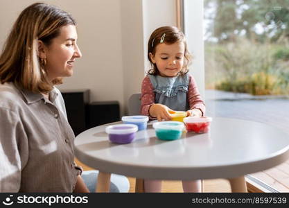 family, creativity and craft concept - mother and little daughter playing with modeling clay at home. mother and daughter playing with modeling clay