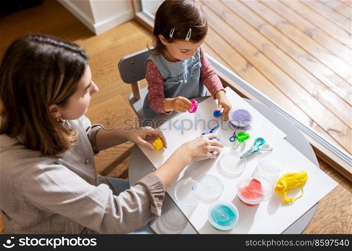 family, creativity and craft concept - mother and little daughter playing with modeling clay at home. mother and daughter playing with modeling clay