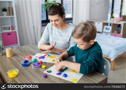 family, creativity and craft concept - mother and little son making picture of modeling clay at home. mother and son playing with modeling clay at home