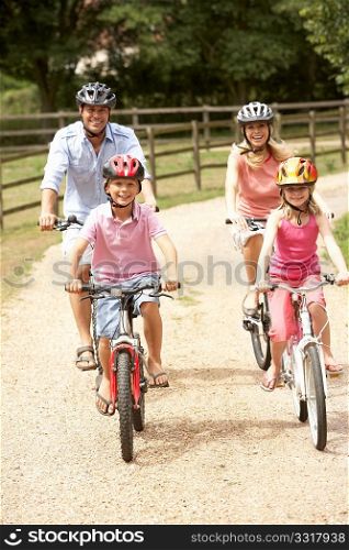 Family Cycling In Countryside Wearing Safety Helmets