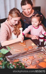 Family decorating baked Christmas gingerbread cookies with frosting