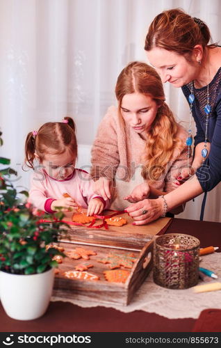 Family decorating baked Christmas gingerbread cookies with frosting