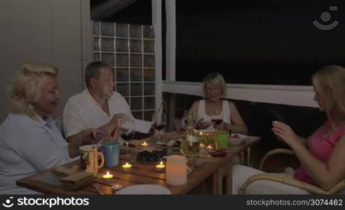 Family dinner on the balcony in late evening. People busy with smart phones and laptop, young woman taking some pictures. They dont have time to talk with each other