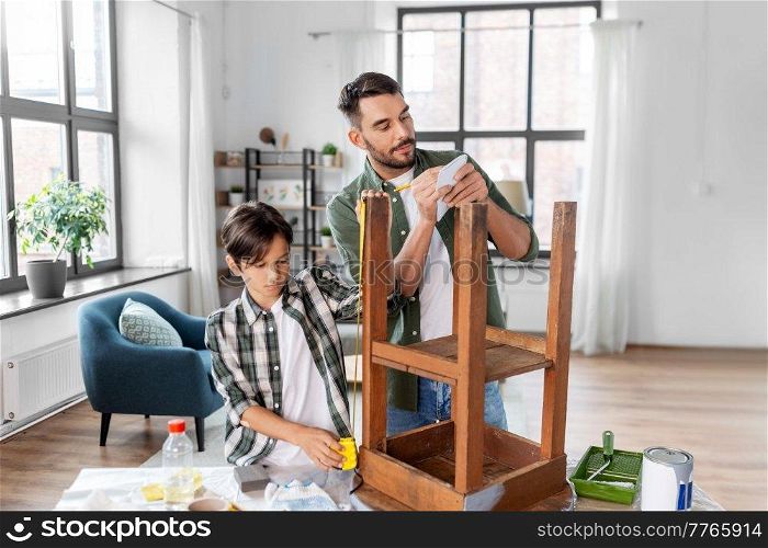 family, diy and home improvement concept - father and son with ruler measuring old round wooden table for renovation at home. father and son with ruler measuring old table