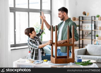family, diy and home improvement concept - happy smiling father and son restoring old table and making high five gesture at home. father and son making high five and restore table