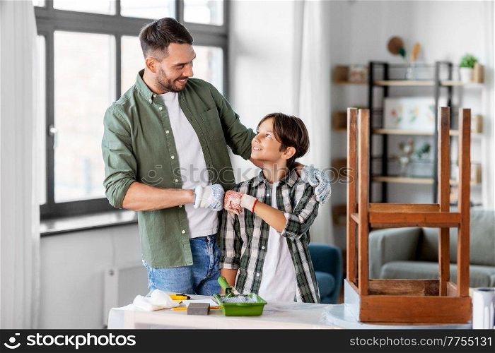family, diy and home improvement concept - happy smiling father and son in gloves restoring old table and making fist bump gesture. father and son making fist bump and restore table