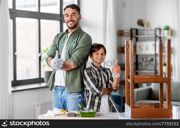 family, diy and home improvement concept - happy smiling father and son showing thumbs up and restoring old table. father and son restoring old table at home