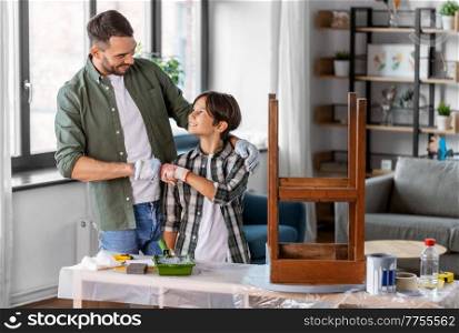 family, diy and home improvement concept - happy smiling father and son in gloves restoring old table and making fist bump gesture at home. father and son making fist bump and restore table