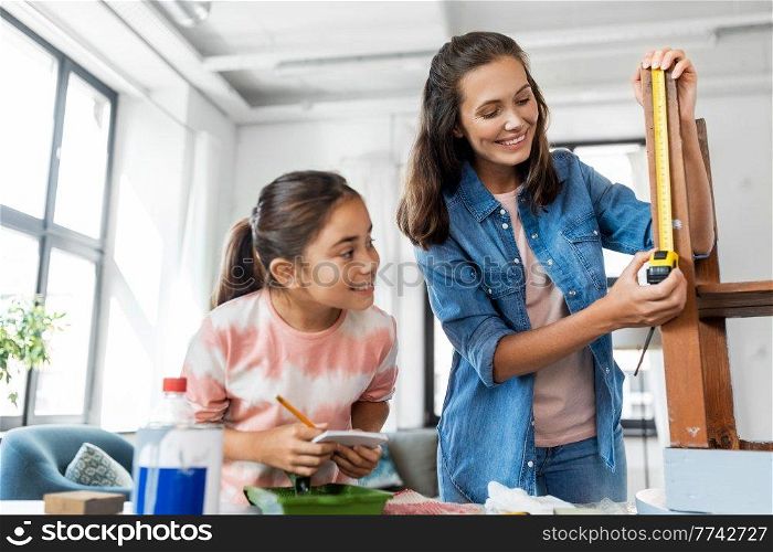 family, diy and home improvement concept - happy smiling mother and daughter with ruler measuring old wooden table for renovation at home. mother and daughter with ruler measuring old table
