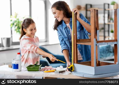 family, diy and home improvement concept - happy smiling mother and daughter with ruler measuring old wooden table for renovation at home. mother and daughter with ruler measuring old table