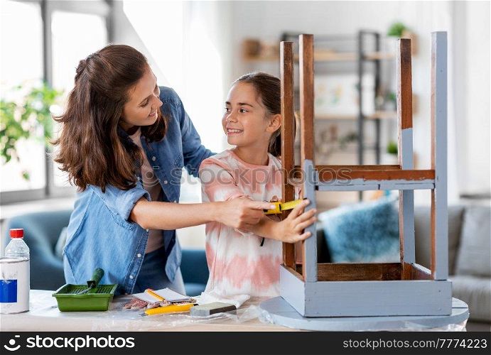 family, diy and home improvement concept - happy smiling mother and daughter with ruler measuring old wooden table for renovation at home. mother and daughter with ruler measuring old table