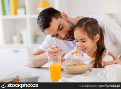 family, eating and people concept - happy father and daughter eating flakes breakfast at home. happy family eating flakes for breakfast at home