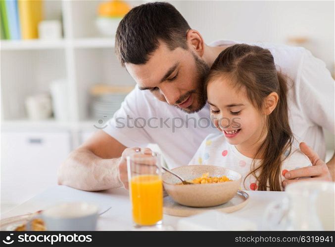 family, eating and people concept - happy father and daughter eating flakes breakfast at home. happy family eating flakes for breakfast at home