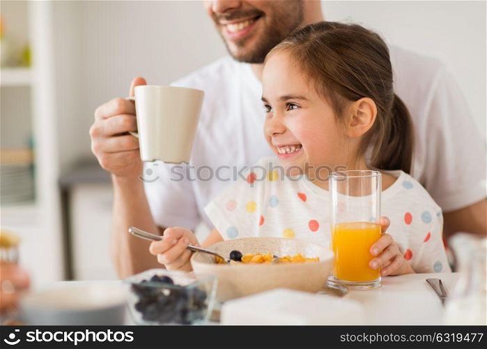 family, eating and people concept - happy father and daughter having breakfast at home. happy family drinking juice for breakfast at home