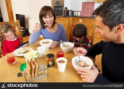 Family Eating Breakfast Together In Kitchen Whilst Children Play With Gadgets