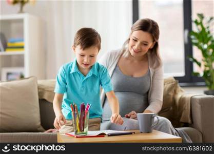 family, education and pregnancy concept - happy pregnant mother and little son with workbook writing or drawing at home. pregnant mother and son with workbook at home