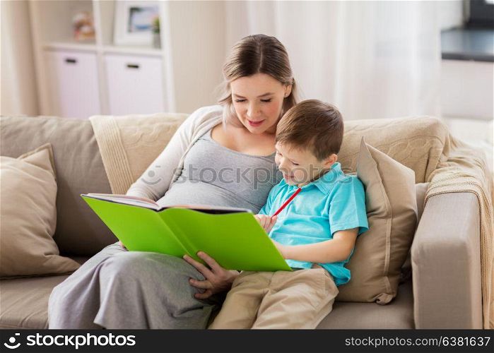family, education and pregnancy concept - happy pregnant mother and little son with book and pencil at home. pregnant mother and little son with book at home
